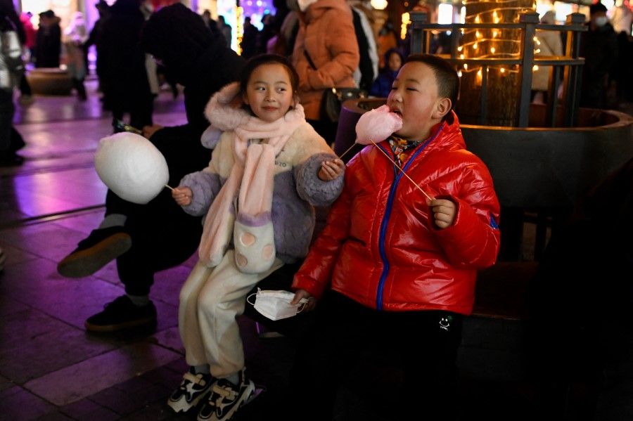 Two children eat candy along a business street during the Chinese Lunar New Year in Beijing on 25 January 2023. (Wang Zhao/AFP)