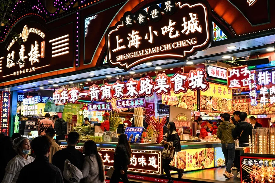 People walk past shops selling food on a pedestrian street in the Huangpu district in Shanghai on 10 November 2025. (Hector Retamal/AFP)