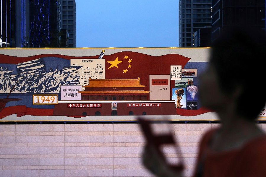 A woman walks past a decorated board with images of Tiananmen Gate and the Chinese national flag, marking the 100th founding anniversary of the Communist Party of China, at a hi-tech industrial park in Beijing, China, 23 June 2021. (Tingshu Wang/Reuters)