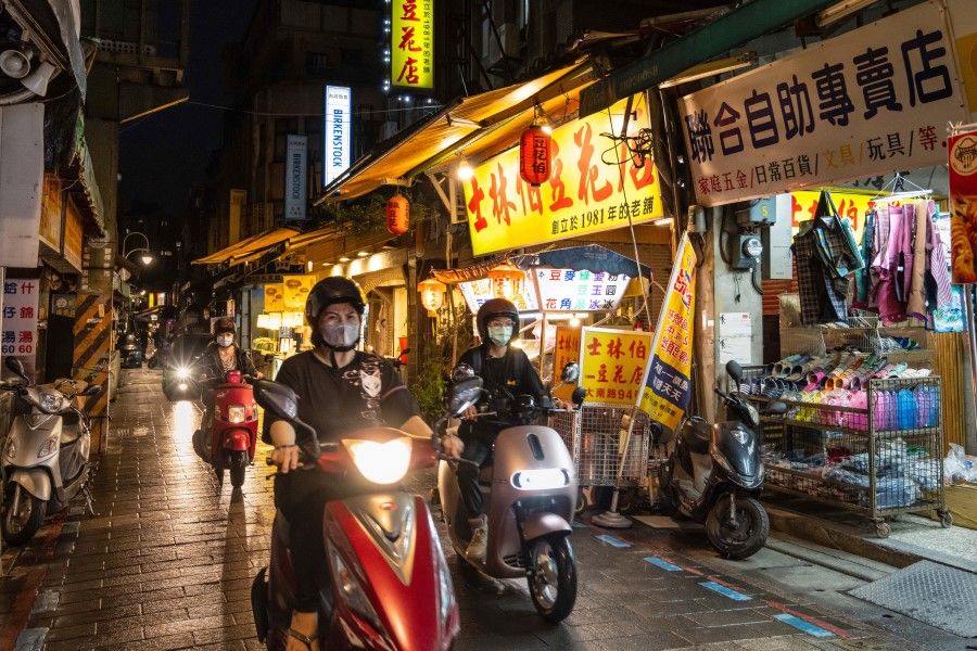 Motorists wearing protective masks ride past stores at a night market in Taipei, Taiwan on 3 June 2021. (Billy H.C. Kwok/Bloomberg)