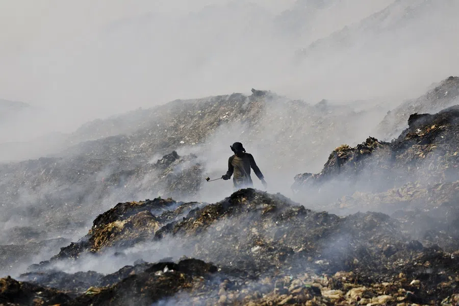 A scavenger searches for recyclable items as smoke billows from burning garbage at the Jatiwaringin landfill site in Tangerang, Banten province, Indonesia, on 1 July 2026.