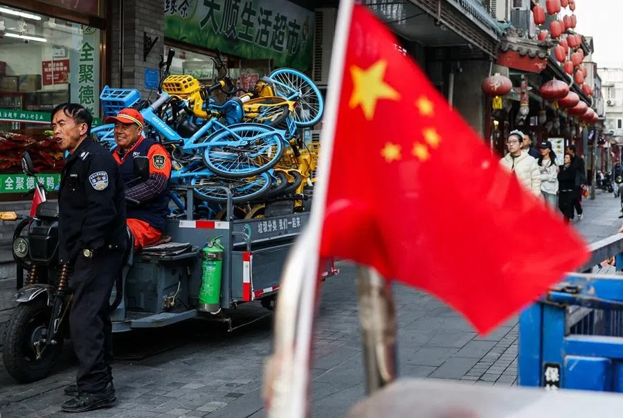 People react next to the national flag of China in a street at a hutong area nearby Qianmen Gate in Beijing, China, on 23 October 2025.
