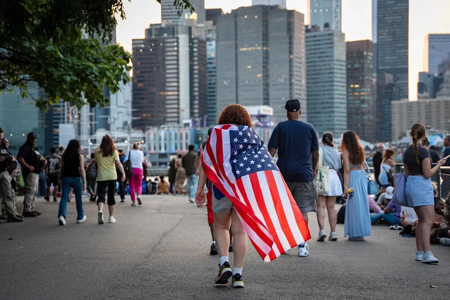 A person drapes a US flag like a cape while crowds gather for the Macy’s Fourth of July fireworks celebration along the East River at Brooklyn Bridge Park in New York on 4 July 2025.