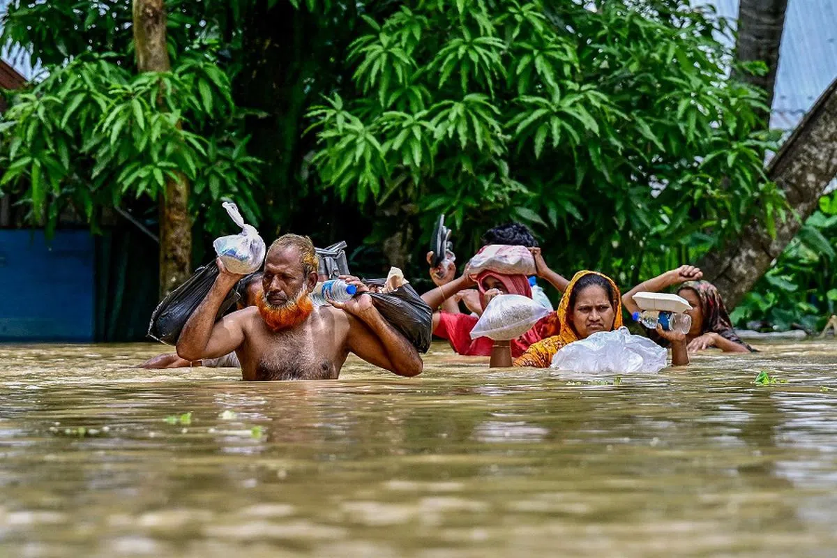 People carrying relief materials wade through flood waters in Feni, in south-eastern Bangladesh, on 24 August 2024. Nearly 300,000 Bangladeshis were taking refuge in emergency shelters on 24 August from floods that inundated vast areas of the low-lying South Asian country, disaster officials said. The floods were triggered by heavy monsoon rains and have killed at least 42 people in Bangladesh and India since the start of the week, many in landslides.