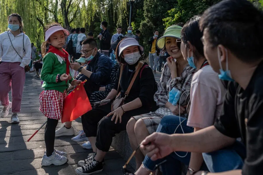 A girl holding a national flag watches as her family chats sitting outside the Forbidden City during the Labour Day holiday in Beijing on 1 May 2021. (Nicolas Asfouri/AFP)