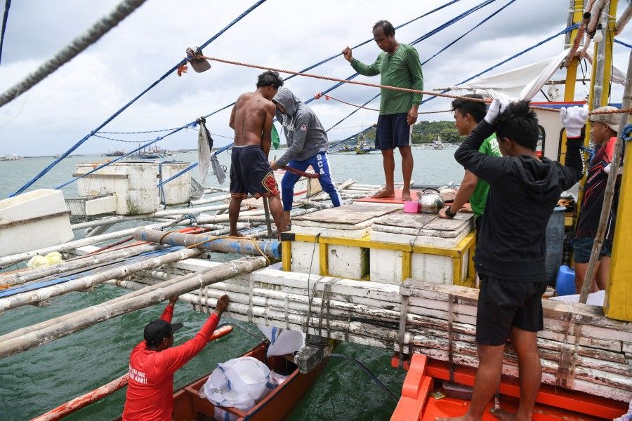In this photo taken on 10 August 2022, fishermen load ice and provisions to their fishing "mother" boat in the village of Cato, Infanta town, Pangasinan province, as they prepare to leave for a fishing expedition to the South China Sea. The Scarborough Shoal fishing ground, tapped by generations of Filipino fishermen, is one of many potential flashpoints for military conflict over the South China Sea. (Ted Aljibe/AFP)