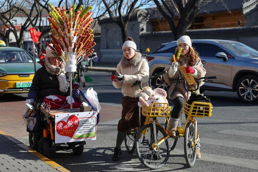 Two Chinese women buy sweet candy sticks from a street vendor in Beijing on 2 December 2025. (Ludovic Marin/AFP)