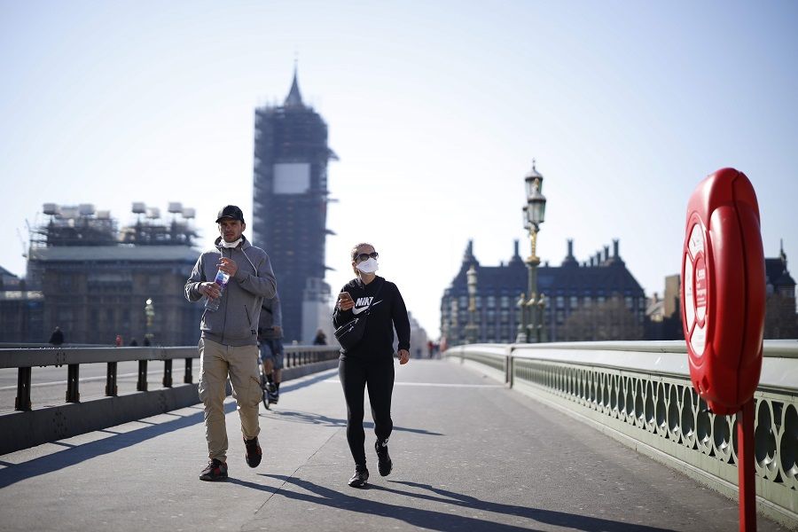 Pedestrians in masks walk along Westminster Bridge with Big Ben in the background, in a quiet central London on 25 March 2020. (Tolga Akmen/AFP)