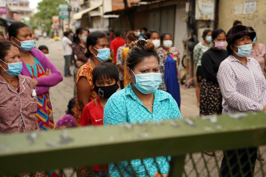 A woman stands with her neighbours behind a lockdown barrier after their village has been closed for more than two weeks inside a red zone with strict lockdown measures during the latest outbreak of the coronavirus disease (Covid-19) in Phnom Penh, Cambodia, 30 April 2021. (Cindy Liu/Reuters)
