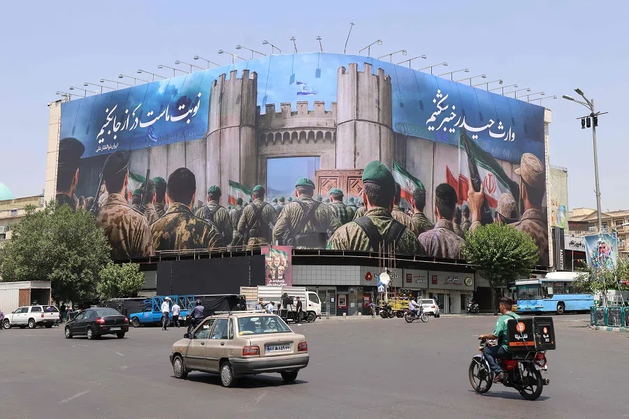 Iranians drive past an anti-Israel poster in Tehran’s Enghelab Square on 14 June 2025. (Atta Kenare/AFP)
