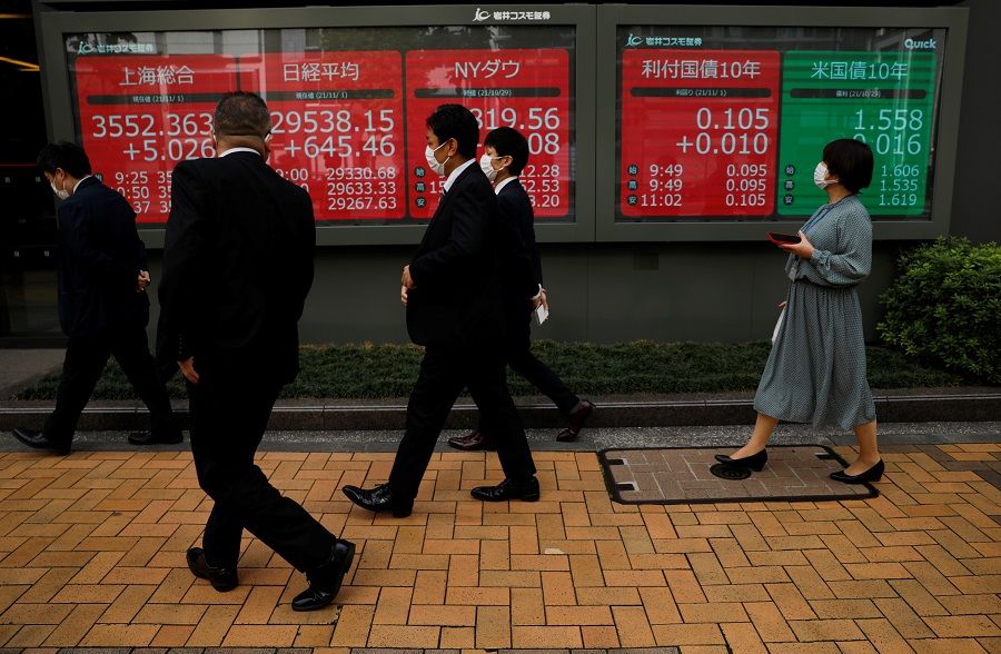 Passersby wearing protective face masks walk past an electronic board displaying world stock indexes, in Tokyo, Japan, 1 November 2021. (Issei Kato/Reuters)