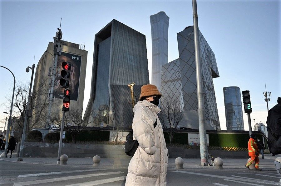 A woman crosses a road in the central business district in Beijing, China, on 16 December 2021. (Greg Baker/AFP)