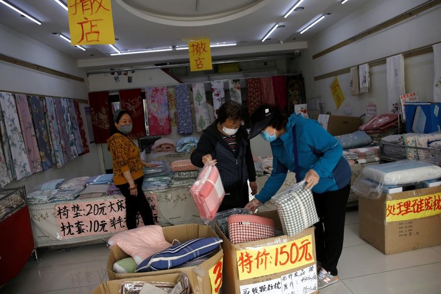 Customers wearing face masks shop bed linen under business closure notices inside a home linen store whose business has been struggling since the Covid-19 outbreak, in Beijing, China, on 14 April 2020. (Tingshu Wang/Reuters)