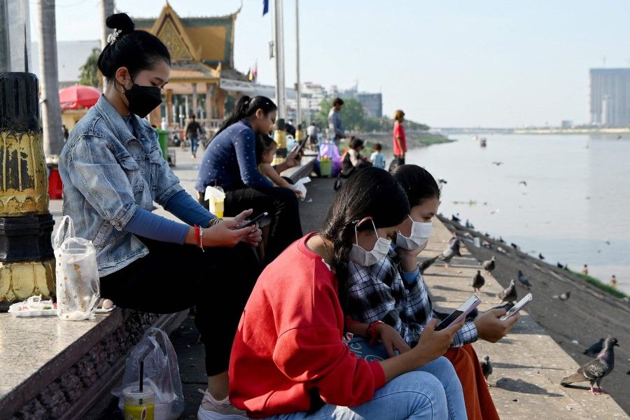 This photo taken on 4 February 2022 shows students using their smartphones while seated along the riverside in Phnom Penh. (Tang Chhin Sothy/AFP)