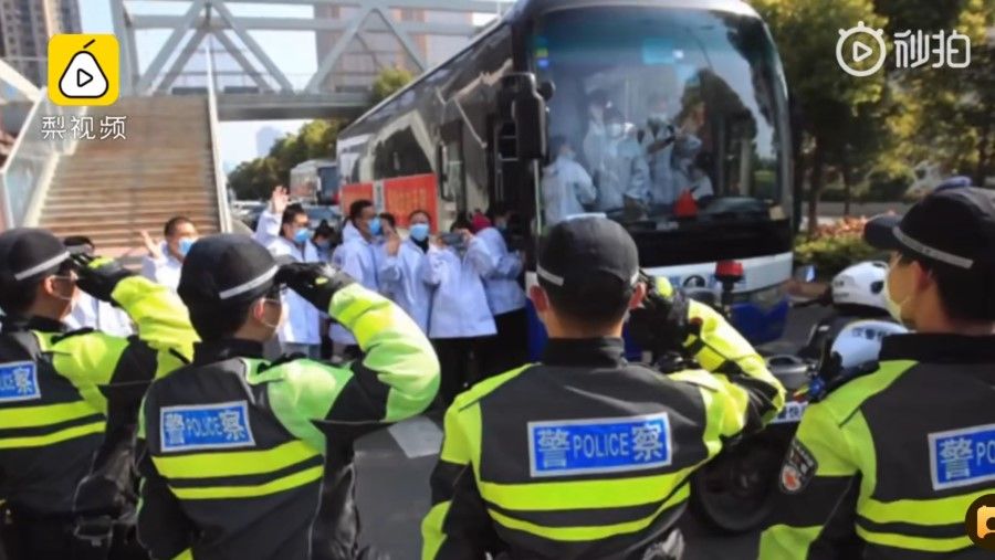 Police salute medical workers as they board a bus. (Screenshot from Weibo video)