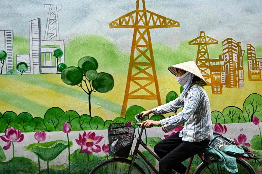 A woman rides her bicycle past a mural showing electricity poles in Hanoi, 19 June 2023. (Nhac Nguyen/AFP)