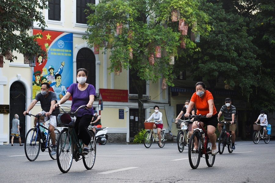 People wearing face masks ride their bicycles on the street in Hanoi, Vietnam, 1 October 2021. (Stringer/Reuters)