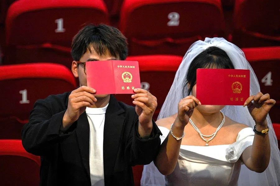 A couple holds up their marriage certificates during a photo session with a local photographer as they visit the Chongqing People’s Auditorium at the Yuzhong district in Chongqing, China, on 11 June 2025.