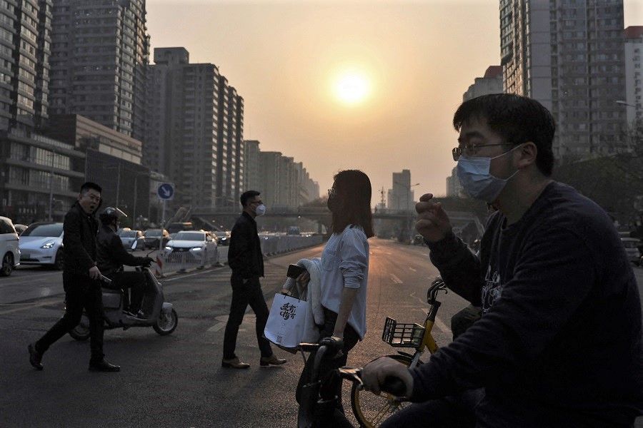 People wearing face masks walk past a street following the Covid-19 outbreak, during rush hour in Beijing, China, 8 April 2022. (Tingshu Wang/Reuters)