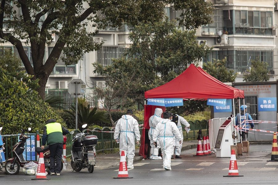 Security guards wearing protective suits walk toward the entrance of a neighbourhood placed under lockdown in Shanghai, China, on 17 December 2021. (Qilai Shen/Bloomberg)