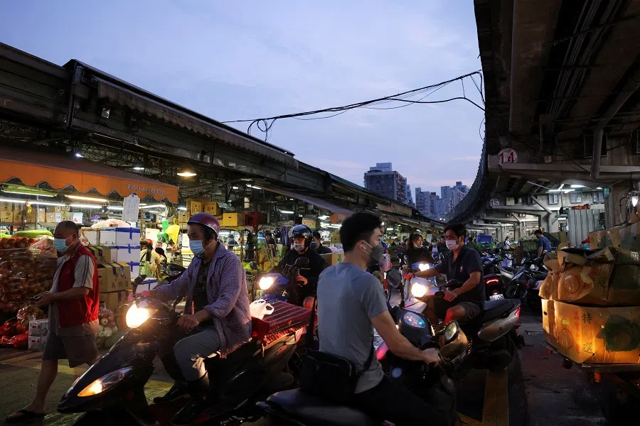 People wearing face masks to prevent the spread of Covid-19 ride past vegetable stalls at a market at dawn in Taipei, Taiwan, 22 April 2022. (Annabelle Chih/Reuters)