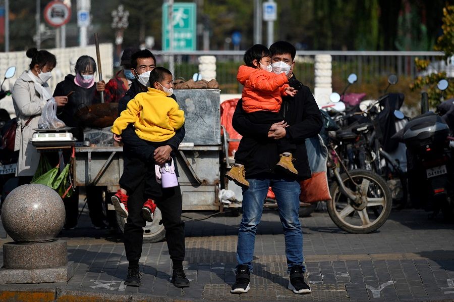 People carrying children wait to cross a street in Beijing, China, on 8 November 2022. (Wang Zhao/AFP)