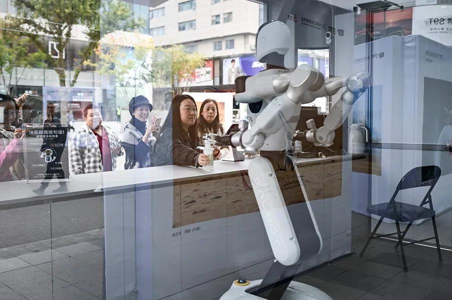 A woman takes a drink from a robot at a booth along a business street in Beijing, China on 22 October 2025. (Wang Zhao/AFP)