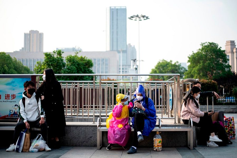 People wearing face masks sit outside Hankou Railway Station in Wuhan in hopes of taking one of the first trains leaving the city early on 8 April 2020. (Noel Celis/AFP)