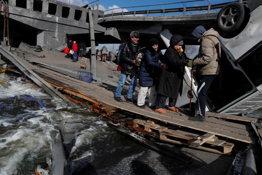 People cross the Irpin river next to a destroyed bridge as they evacuate from the Irpin town, as Russia's attack on Ukraine continues, outside of Kyiv, Ukraine, 10 March 2022. (Valentyn Ogirenko/Reuters)