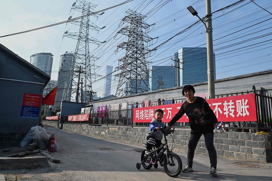 A woman guides a boy learning to cycle below power lines in Beijing, China, on 13 October 2021. (Noel Celis/AFP)