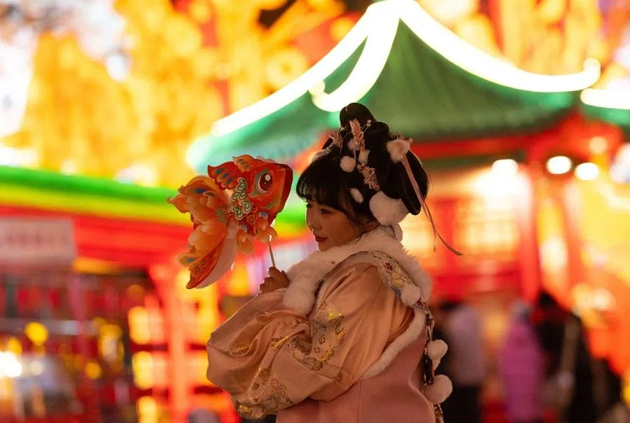 A young woman wearing traditional dress holds a paper fish figure next to light installations at the 32nd Zigong International Lantern Festival, ahead of the Chinese Lunar New Year, in Zigong, Sichuan province, China, 23 January 2026. (Maxim Shemetov/Reuters)