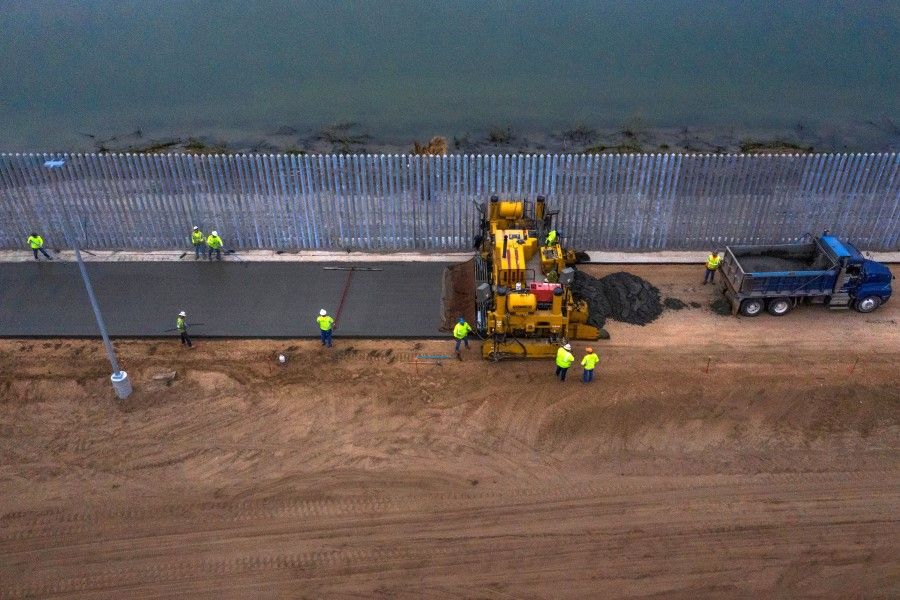A truck drops concrete in front of a paving machine building a road next to a three-mile private border wall along the banks of the Rio Grande river in the town of Mission, Texas, 11 February 2020. (Adrees Latif/REUTERS)