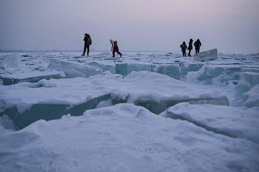People walk on blocks of ice on the frozen Songhua river in Harbin, Heilongjiang province, China, on 6 January 2023. (Hector Retamal/AFP)