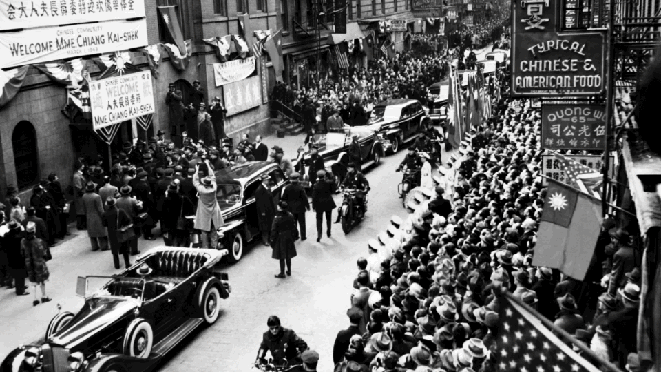 Colouring brings the scene to life. In this image, Madame Chiang (Soong Mei-ling), wife of Chiang Kai-shek, the first president of the Republic of China, visiting a Chinese school in Mott Street, New York, March 1943. The school was in the heart of Chinatown, the earliest Chinese area. Police escort Madame Chiang and her group from the car to the school, surrounded by journalists taking photos. The school has prepared welcome banners as well as the Republic of China flag.