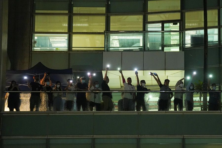 Staff light their phone flashlights and wave to supporters at the headquarters of the Apple Daily newspaper, and its publisher Next Digital, after the announcement that it will print its last edition, in Hong Kong, China, 23 June 2021. (Lam Yik/Reuters)