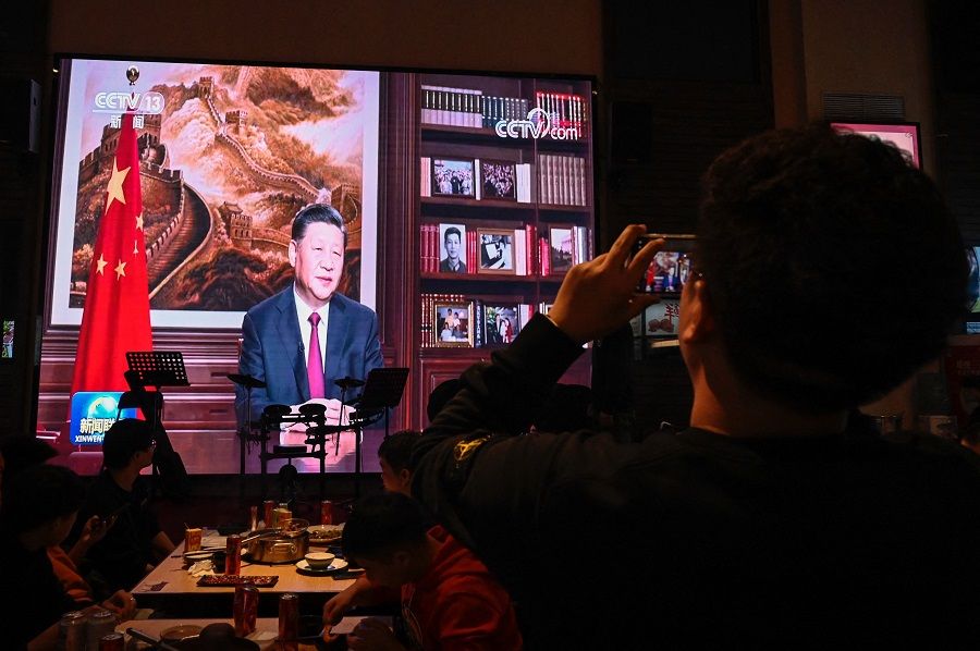 A man takes a photo of a screen broadcasting Chinese President Xi Jinping delivering his New Year speech, at a restaurant in Beijing, China, on 31 December 2021. (Jade Gao/AFP)