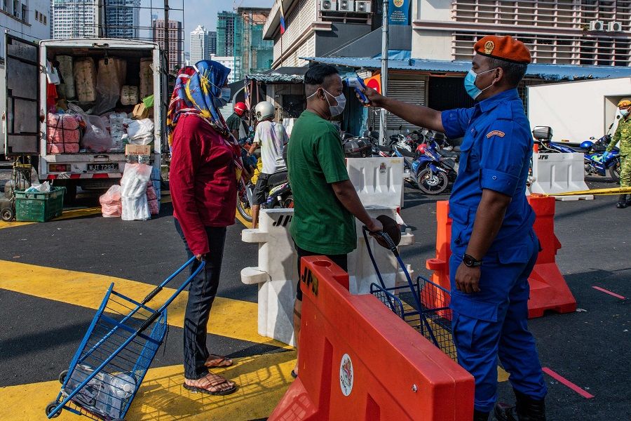 A member of the Malaysia Civil Defence Force checks the temperature of a man before entering the Chow Kit Market in Kuala Lumpur on 17 June 2020. (Mohd Rasfan/AFP)