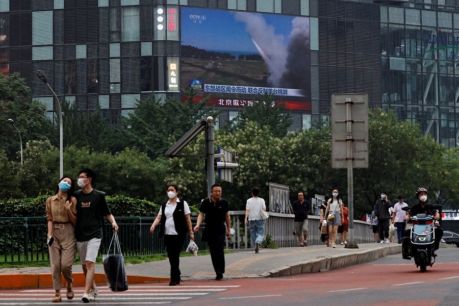 Pedestrians walk past a giant screen broadcasting a news report on Chinese People's Liberation Army's (PLA) military exercises around Taiwan, in Beijing, China, 4 August 2022. (Thomas Peter/File Photo/Reuters)