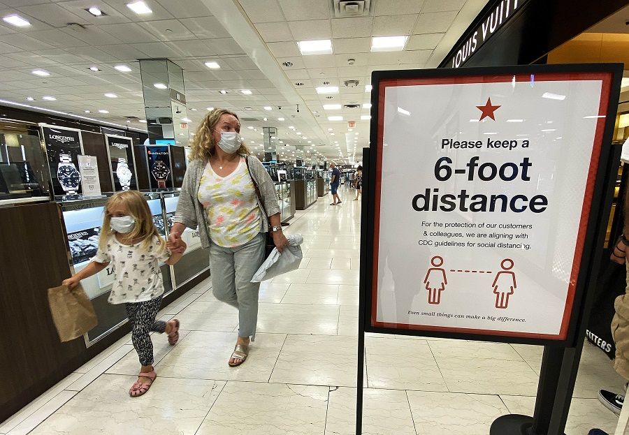 Customers walk past a sign that encourages people to keep a six foot distance from each other at Roosevelt Field Mall which reopened on 10 July 2020 in Garden City, New York. ( Al Bello/Getty Images/AFP)