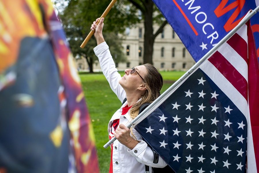 A woman waves a US flag and a flag in support of Donald Trump at the Michigan State Capitol on 12 October 2021 in Lansing, Michigan, US. (Nic Antaya/Getty Images/AFP)