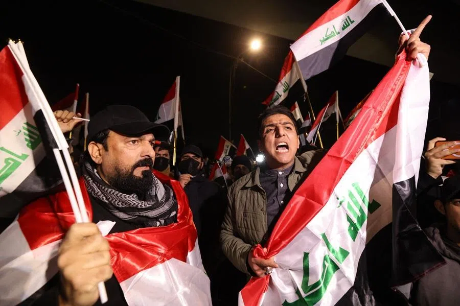 Iraqis raise their flags during a protest at the entrance to the Hanging Bridge, one of the entrances to the Green Zone in Baghdad on 28 January 2026.