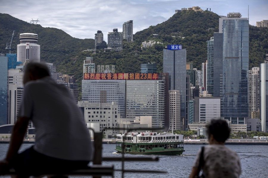 People sit by the Tsim Sha Tsui waterfront as a digital billboard atop the China Evergrande Centre building, center, displays a message celebrating the 23rd anniversary of Hong Kong's handover to China, in Hong Kong, 29 June 2020. (Paul Yeung/Bloomberg)