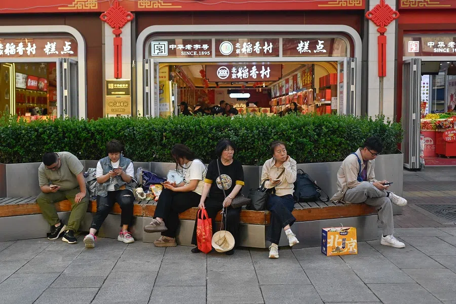 People rest on a bench along a business street in Beijing on 24 September 2024. (Wang Zhao/AFP)