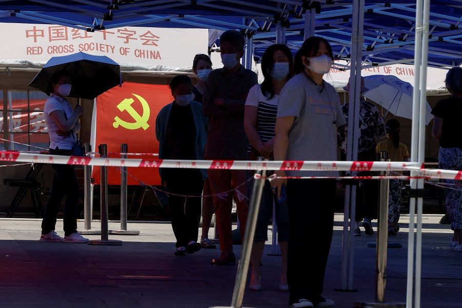 People wearing face masks queue to get tested at a makeshift nucleic acid testing site with the flag of the Communist Party of China displayed, amid the Covid-19 outbreak in Beijing, China, 27 May 2022. (Carlos Garcia Rawlins/Reuters)
