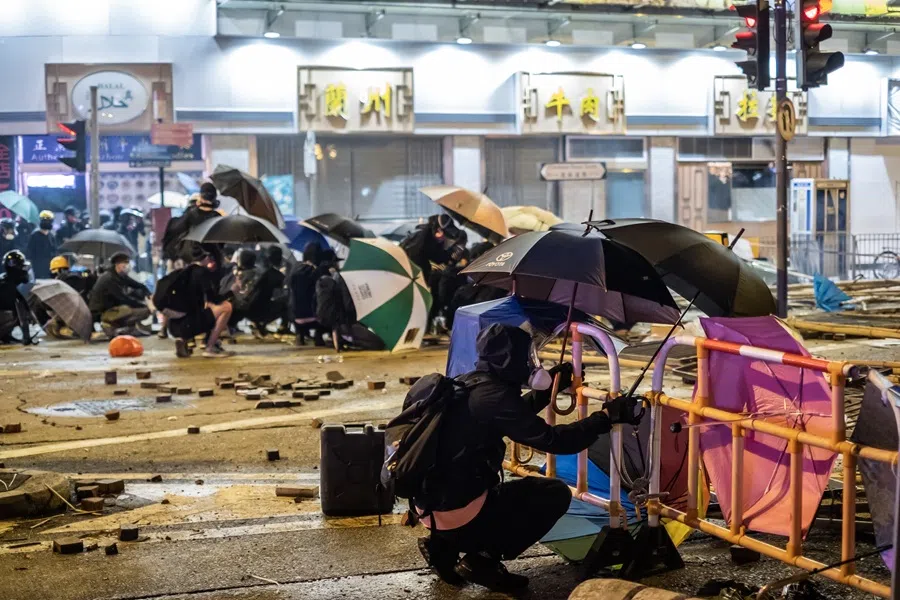Demonstrators kneel behind umbrellas and barricades while standing off against riot police during a protest in the Tsim Sha Tsui district of Hong Kong, China, on 18 November 2019. (Justin Chin/Bloomberg)