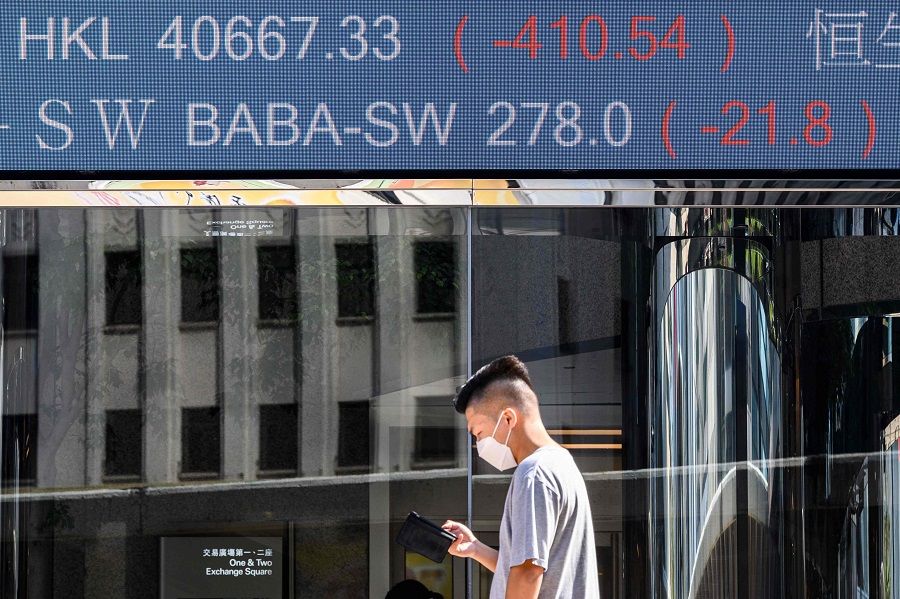 Stock activity of the Alibaba Group Holding Ltd (BABA-SW) (top) is displayed above a man as he looks at his phone while standing outside the Exchange Square towers in Hong Kong on 4 November 2020, after a last minute decision to suspend the record-breaking IPO of fintech giant Ant Group the night before. (Anthony Wallace/AFP)