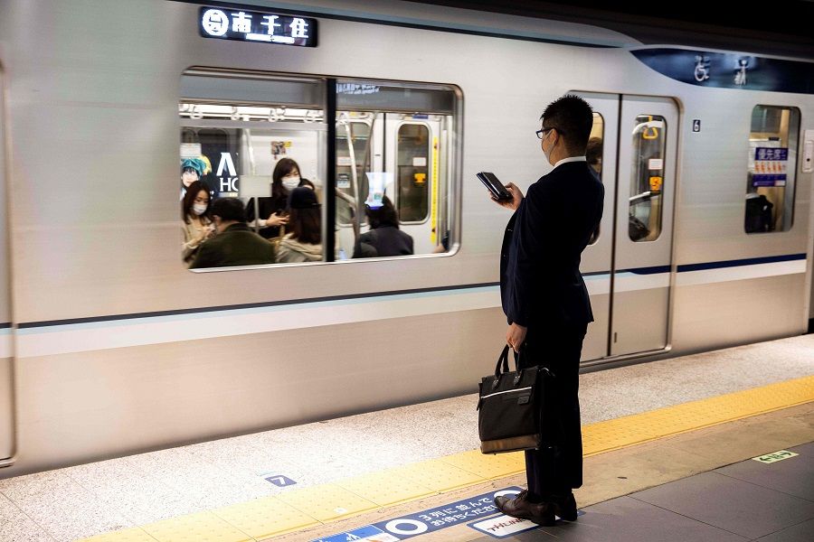 A commuter wearing a face mask checks his phone at Ginza Station in Tokyo on 19 November 2020. (Behrouz Mehri/AFP)