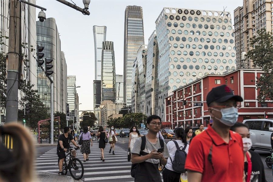 Pedestrians cross a traffic intersection near commercial buildings in Beijing, China, 25 August 2021. (Qilai Shen/Bloomberg)