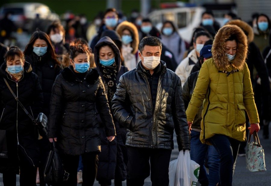 People wearing face masks walk along a street during a rush hour in Bejing on 16 December 2020. (Noel Celis/AFP)