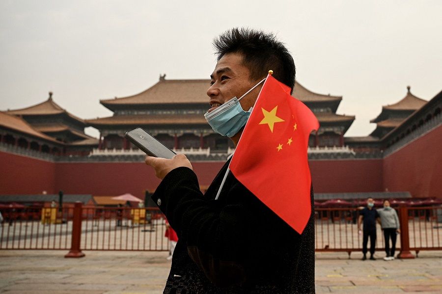 A man holds the Chinese national flag at the entrance of the Forbidden City in Beijing, China, on 1 October 2022. (Noel Celis/AFP)
